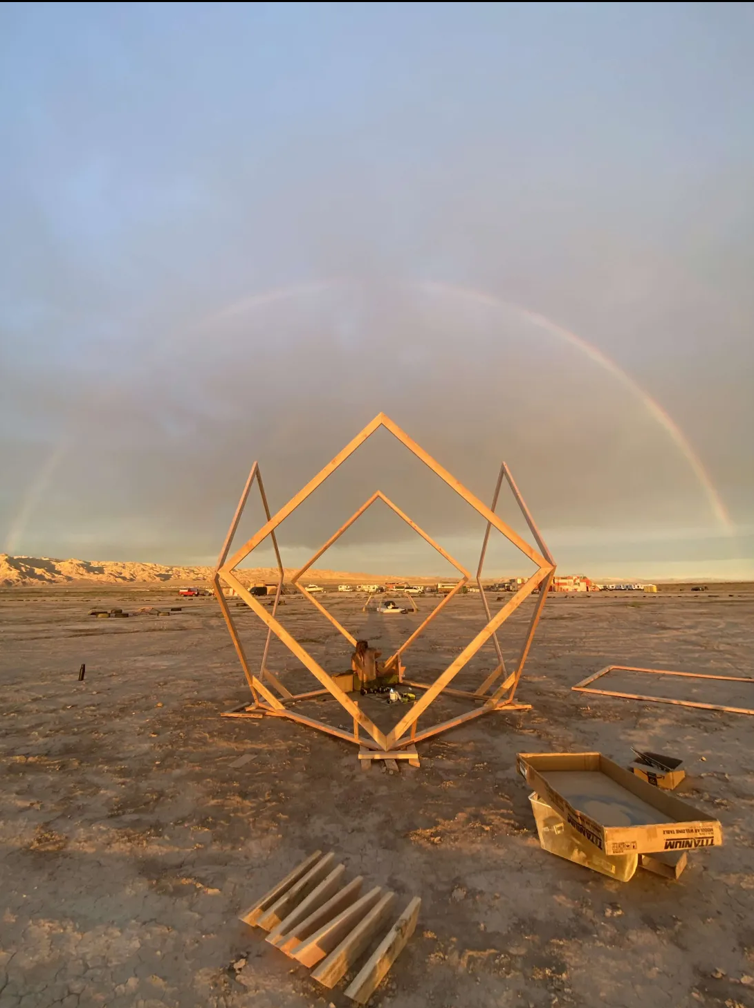 Geometric wooden sculpture beneath a desert rainbow