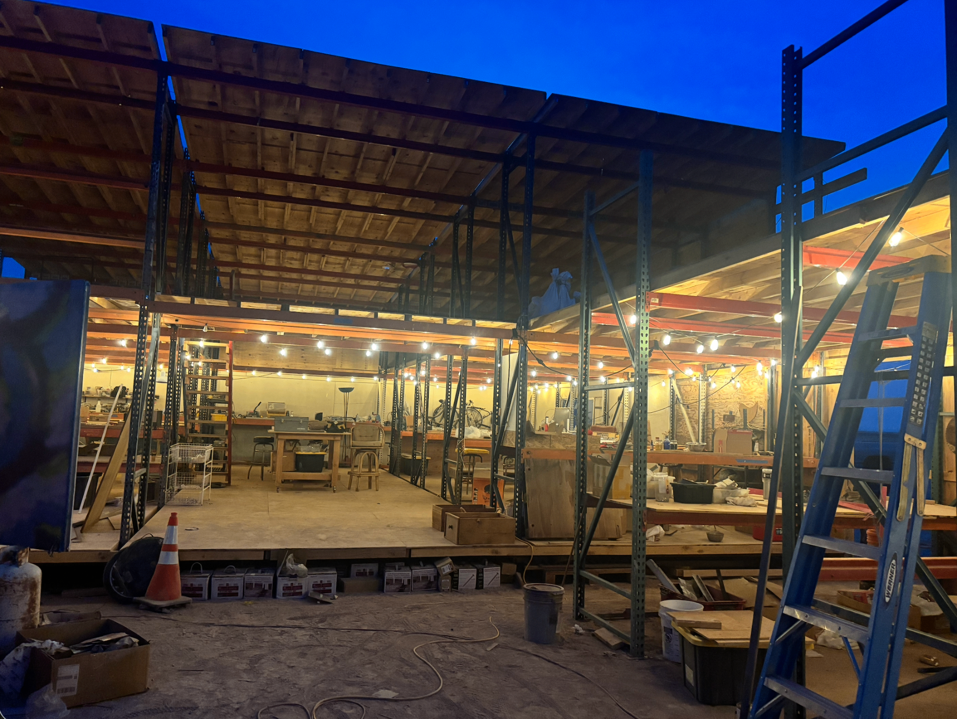 The workshop at dusk, lit with string lights under a deep blue sky